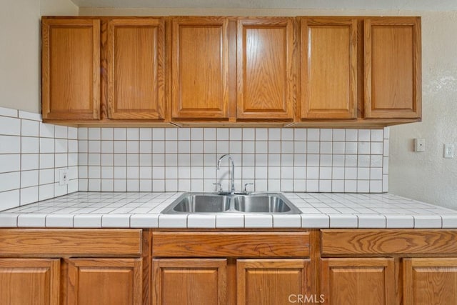 kitchen with decorative backsplash, light countertops, brown cabinets, and a sink