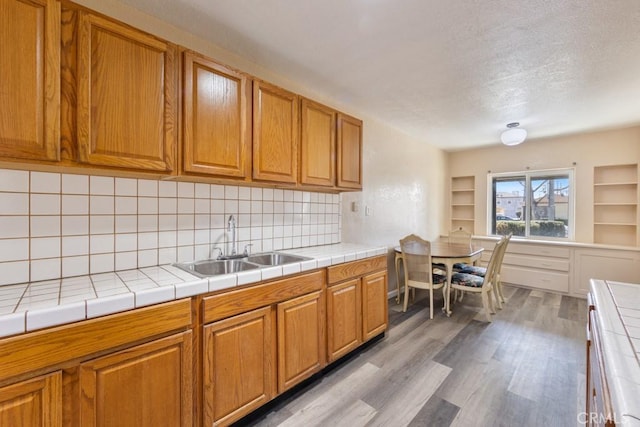 kitchen with backsplash, light wood-style flooring, brown cabinetry, a textured ceiling, and a sink