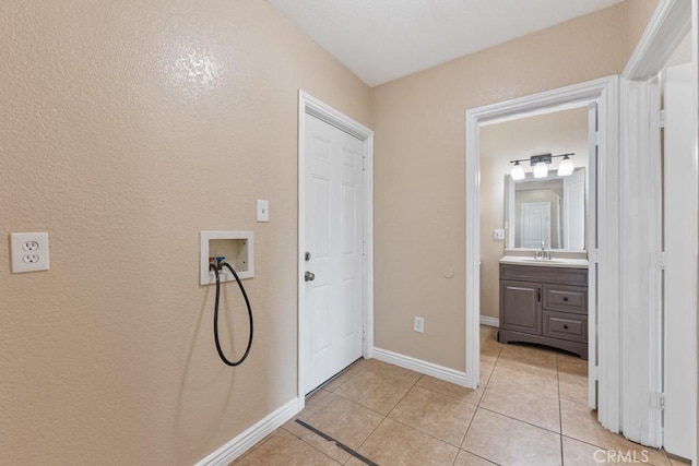 clothes washing area with washer hookup, a sink, light tile patterned floors, baseboards, and laundry area