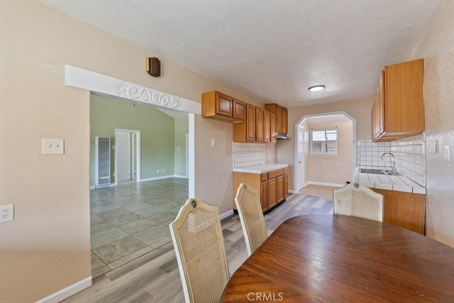 kitchen with decorative backsplash, tile counters, brown cabinets, and a sink