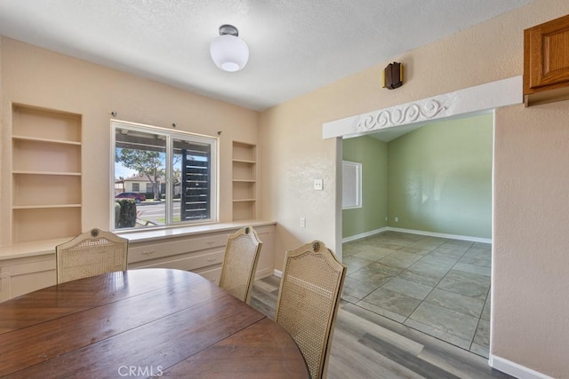 dining area featuring built in shelves, a textured ceiling, wood finished floors, baseboards, and a textured wall