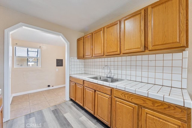 kitchen with a sink, tasteful backsplash, tile countertops, arched walkways, and baseboards