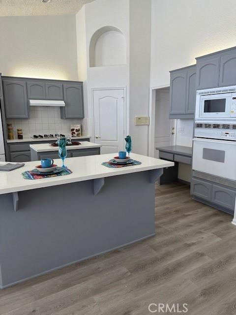 kitchen featuring a breakfast bar area, gray cabinetry, wood-type flooring, and white appliances