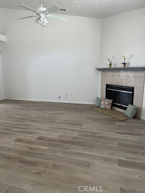 unfurnished living room with a fireplace, ceiling fan, wood-type flooring, and a textured ceiling