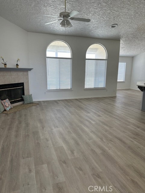 unfurnished living room featuring a tile fireplace, ceiling fan, light hardwood / wood-style floors, and a textured ceiling