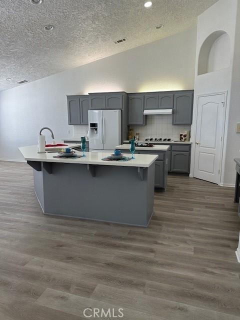 kitchen featuring a textured ceiling, white fridge with ice dispenser, gray cabinetry, and a kitchen island with sink