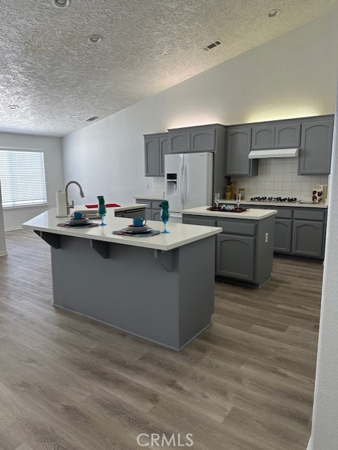 kitchen with a textured ceiling, a kitchen island with sink, white refrigerator with ice dispenser, hardwood / wood-style floors, and gray cabinets