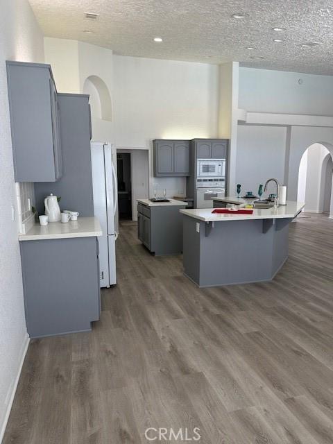 kitchen with a textured ceiling, white appliances, gray cabinets, and dark hardwood / wood-style flooring