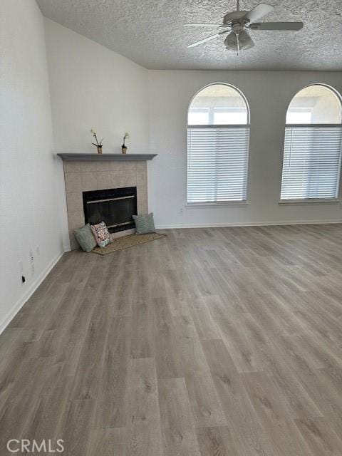 unfurnished living room with a tiled fireplace, ceiling fan, a textured ceiling, and hardwood / wood-style flooring