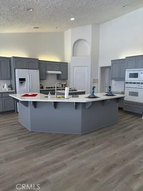 kitchen featuring gray cabinetry, dark wood-type flooring, an island with sink, a textured ceiling, and white appliances