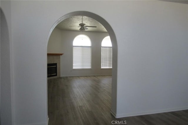 unfurnished living room featuring a tile fireplace, ceiling fan, dark hardwood / wood-style flooring, and a textured ceiling