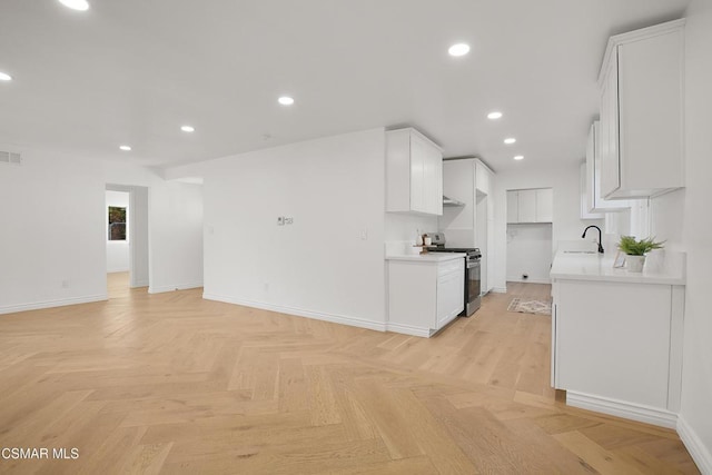 kitchen featuring sink, white cabinetry, stainless steel range oven, and light parquet flooring