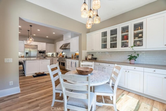 kitchen with built in appliances, white cabinetry, and hanging light fixtures