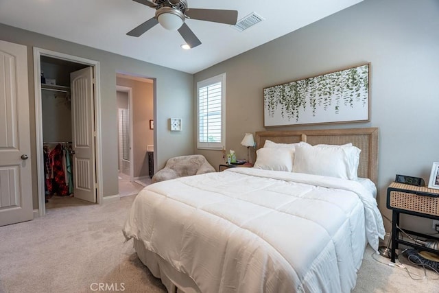 bedroom featuring a closet, light colored carpet, ceiling fan, a walk in closet, and ensuite bathroom