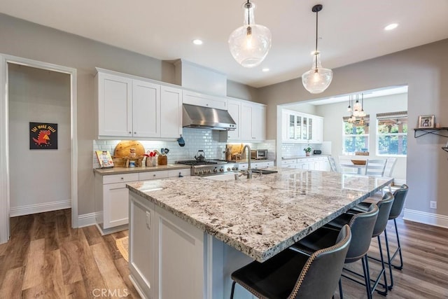 kitchen featuring extractor fan, white cabinets, hanging light fixtures, and an island with sink