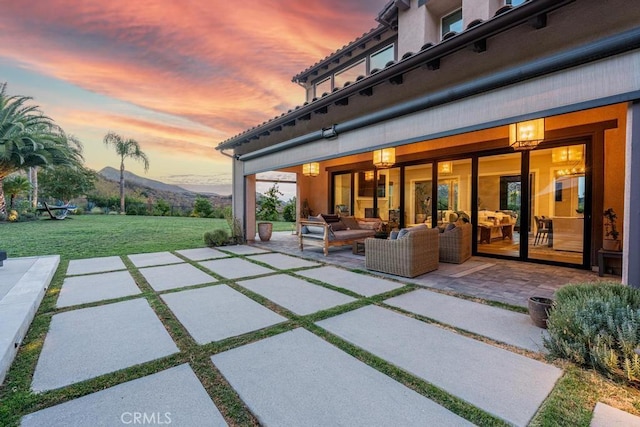 patio terrace at dusk featuring a lawn, a mountain view, and outdoor lounge area