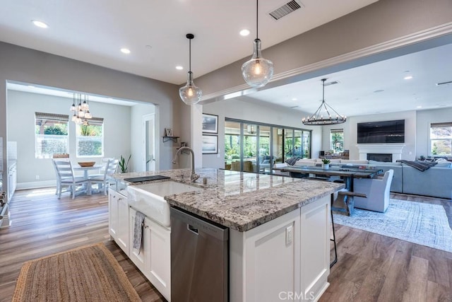 kitchen with sink, white cabinets, stainless steel dishwasher, a center island with sink, and pendant lighting