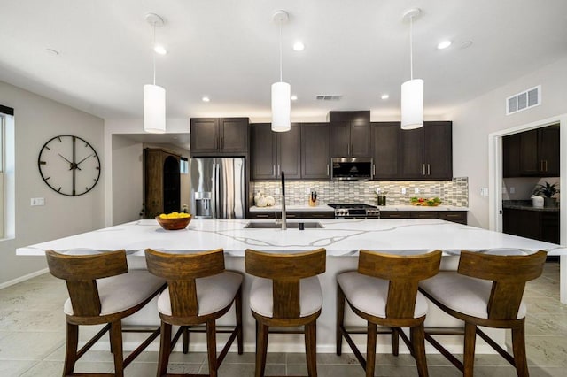 kitchen with a large island with sink, stainless steel appliances, decorative light fixtures, and sink