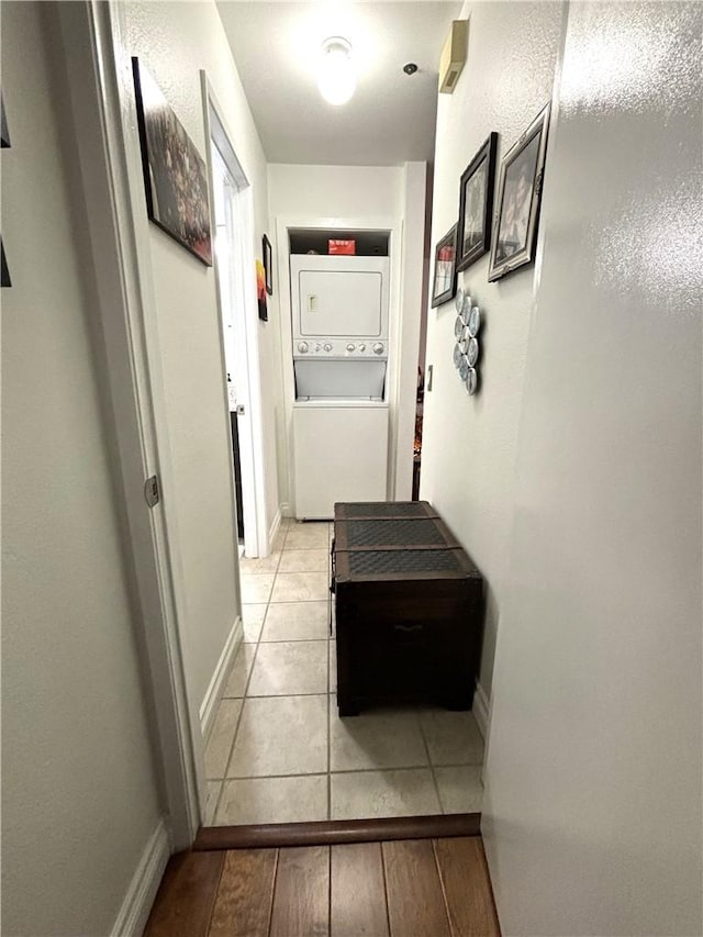 hallway featuring light tile patterned floors, baseboards, and stacked washer / dryer