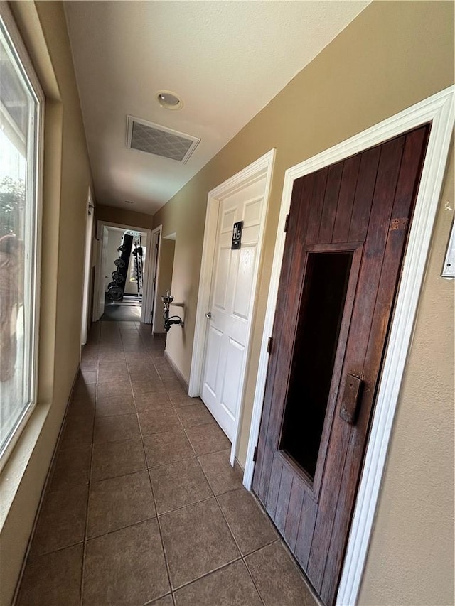 hallway featuring baseboards, visible vents, and dark tile patterned flooring