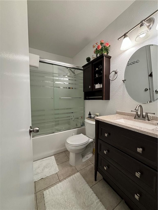 bathroom with a textured wall, toilet, combined bath / shower with glass door, vanity, and tile patterned flooring