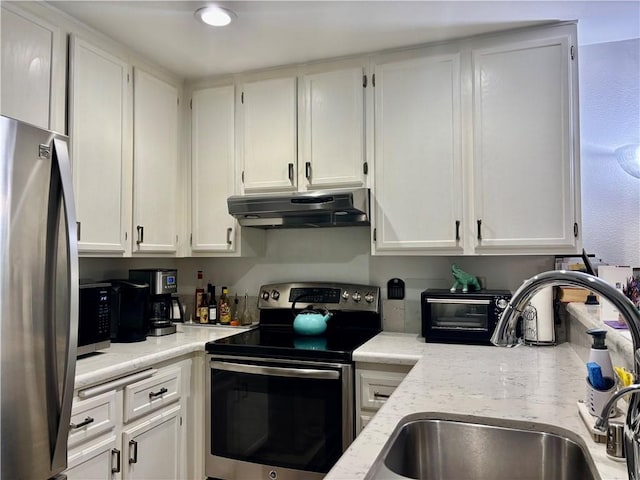 kitchen with white cabinets, light stone counters, appliances with stainless steel finishes, under cabinet range hood, and a sink