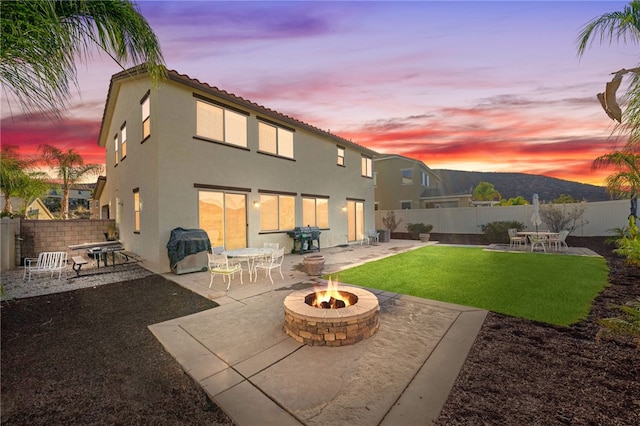 back house at dusk featuring a yard, an outdoor fire pit, and a patio