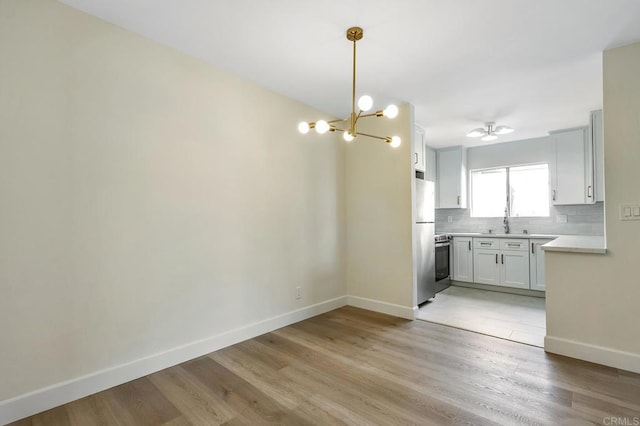 kitchen featuring stainless steel appliances, light hardwood / wood-style floors, decorative light fixtures, decorative backsplash, and white cabinets