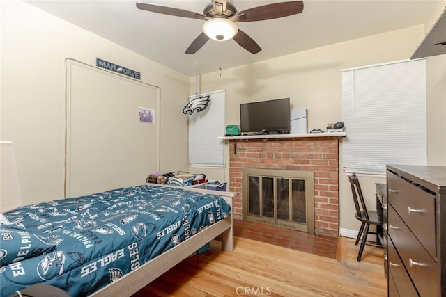 bedroom with ceiling fan, light hardwood / wood-style floors, and a brick fireplace