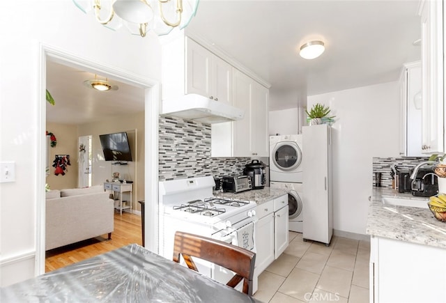 kitchen with decorative backsplash, white gas range oven, sink, stacked washer and clothes dryer, and white cabinets