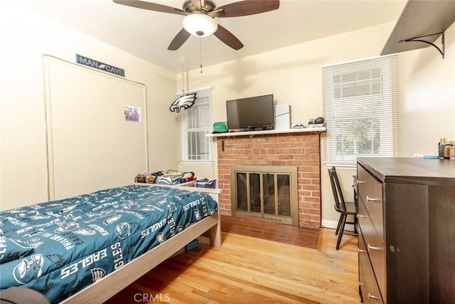 bedroom with a brick fireplace, ceiling fan, and light hardwood / wood-style flooring