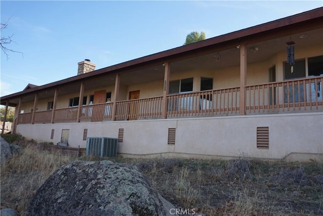 view of side of property with central air condition unit, a chimney, and stucco siding