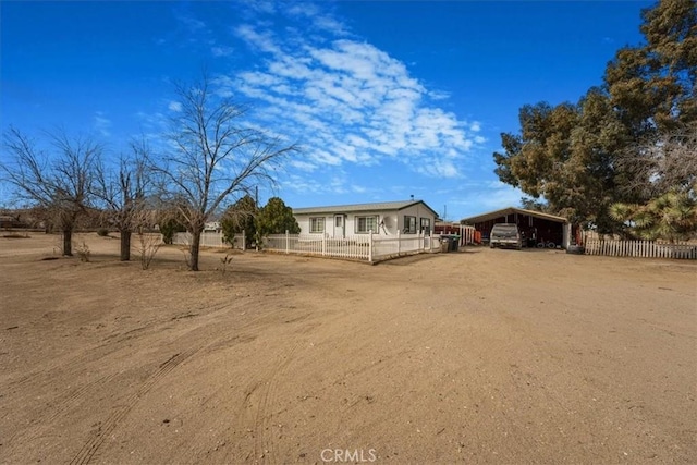 view of yard with dirt driveway, fence, and a detached carport