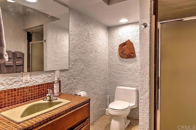 bathroom with decorative backsplash, vanity, a shower with shower door, and toilet