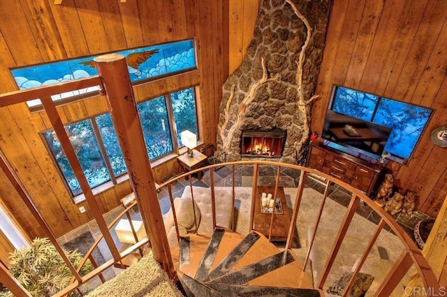 stairs featuring a stone fireplace, wooden walls, and a towering ceiling