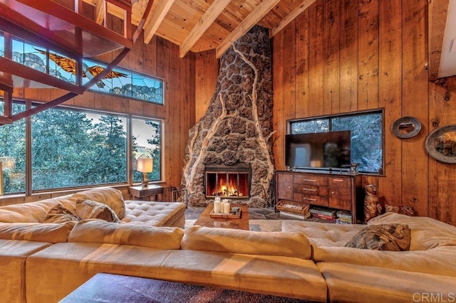 living room featuring beam ceiling, high vaulted ceiling, wooden ceiling, a fireplace, and wood walls