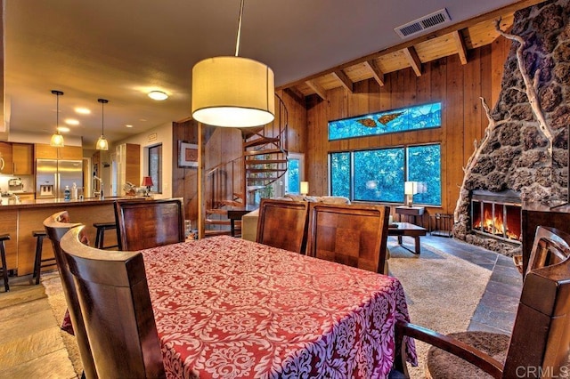 dining area with a stone fireplace, wooden walls, and beamed ceiling