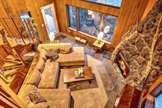 living room with a stone fireplace, a towering ceiling, and wooden walls