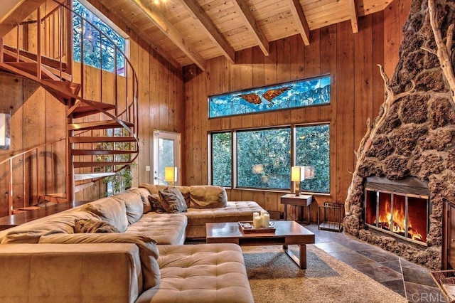 living room featuring wood ceiling, beam ceiling, high vaulted ceiling, a stone fireplace, and wood walls