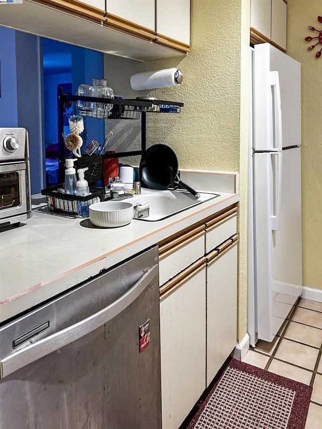 kitchen with dishwasher, light tile patterned floors, white refrigerator, and white cabinetry