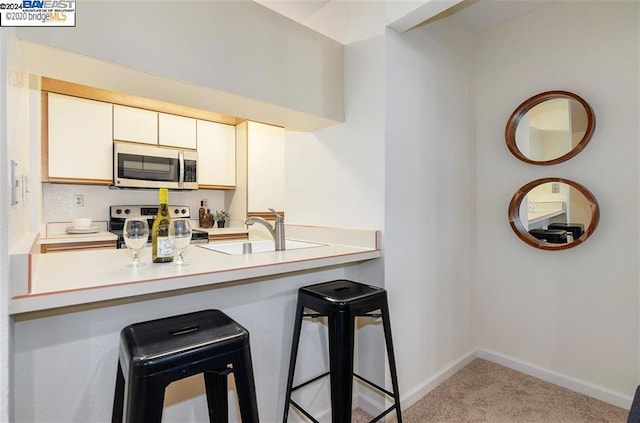 kitchen featuring a breakfast bar, white cabinets, sink, electric range, and light colored carpet