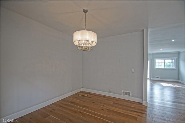 spare room featuring wood-type flooring and an inviting chandelier