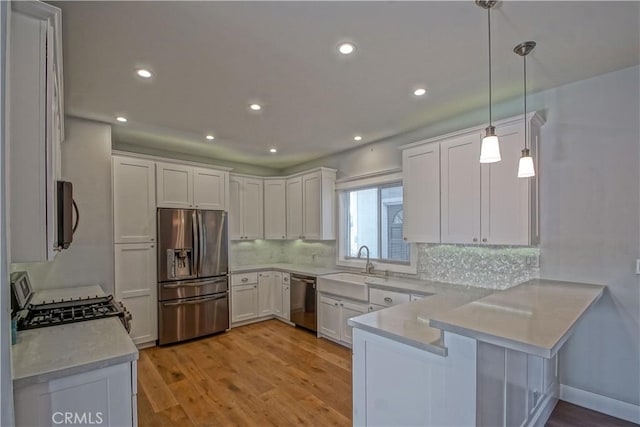 kitchen with kitchen peninsula, appliances with stainless steel finishes, pendant lighting, light hardwood / wood-style flooring, and white cabinets