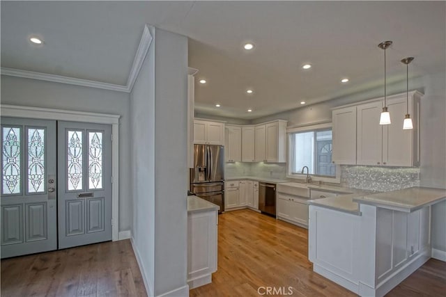 kitchen featuring kitchen peninsula, hanging light fixtures, appliances with stainless steel finishes, light hardwood / wood-style floors, and white cabinetry