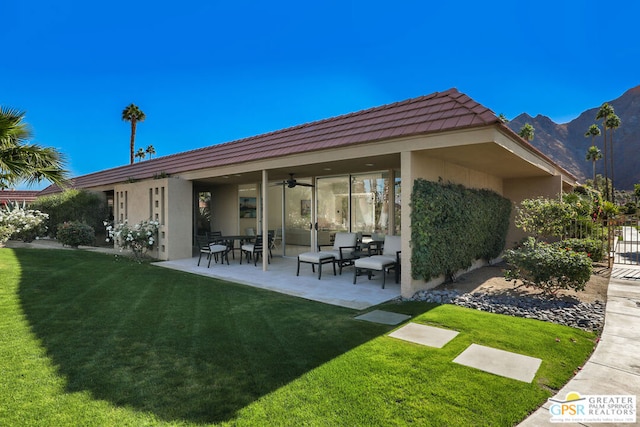 rear view of property with a mountain view, a yard, ceiling fan, and a patio