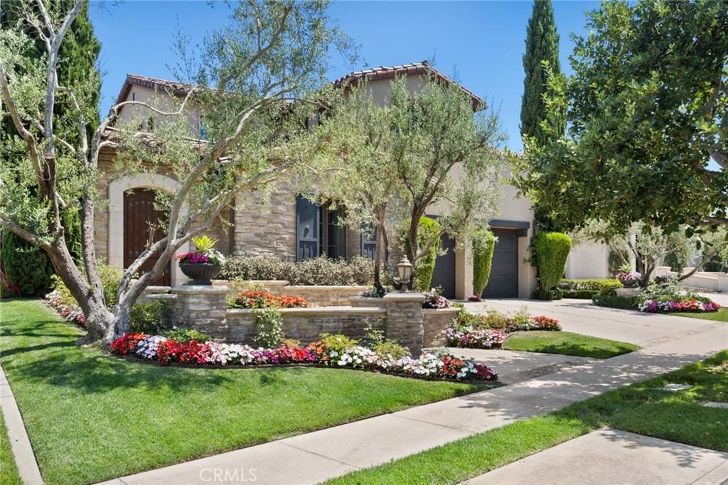 mediterranean / spanish house featuring driveway, an attached garage, stucco siding, a front lawn, and stone siding