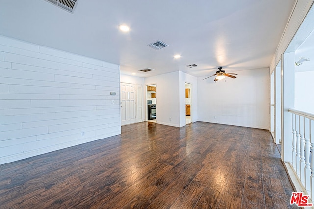 unfurnished living room featuring ceiling fan, dark hardwood / wood-style flooring, and wooden walls