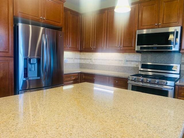 kitchen with light stone countertops, backsplash, and appliances with stainless steel finishes