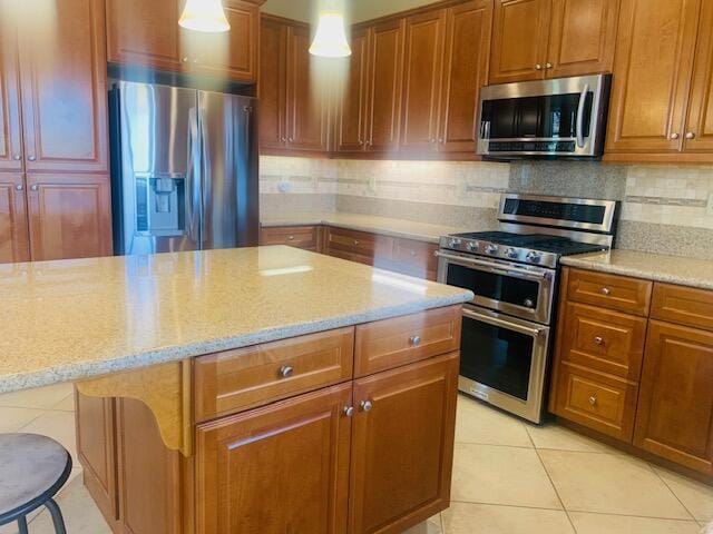 kitchen featuring hanging light fixtures, light tile patterned floors, light stone countertops, appliances with stainless steel finishes, and a breakfast bar area