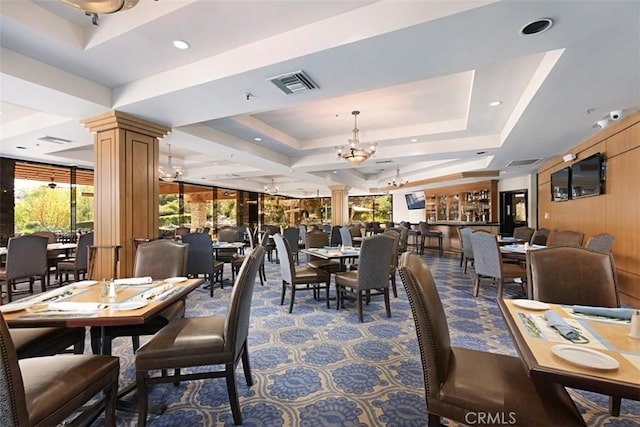 dining room with ornate columns, carpet floors, a raised ceiling, a chandelier, and wood walls